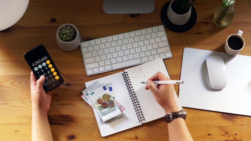 Persona calculando su presupuesto con el móvil y un cuaderno para planificar sus finanzas